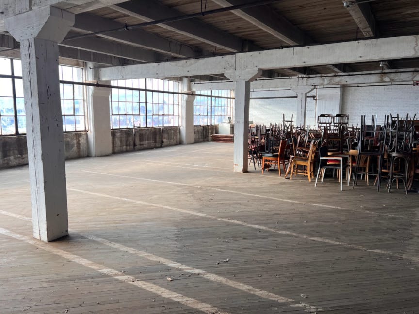 An industrial loft with large windows, exposed beams, and stacked wooden chairs.