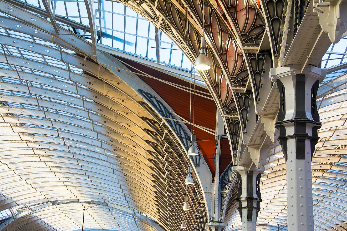 Interior view of Paddington Station in London, featuring ornate iron columns, arched glass roof, and hanging industrial lights, highlighting Victorian architecture and structural detail.