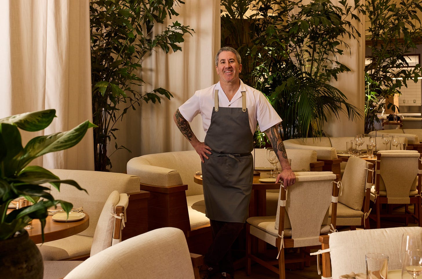 A man in an apron standing in a dining room.