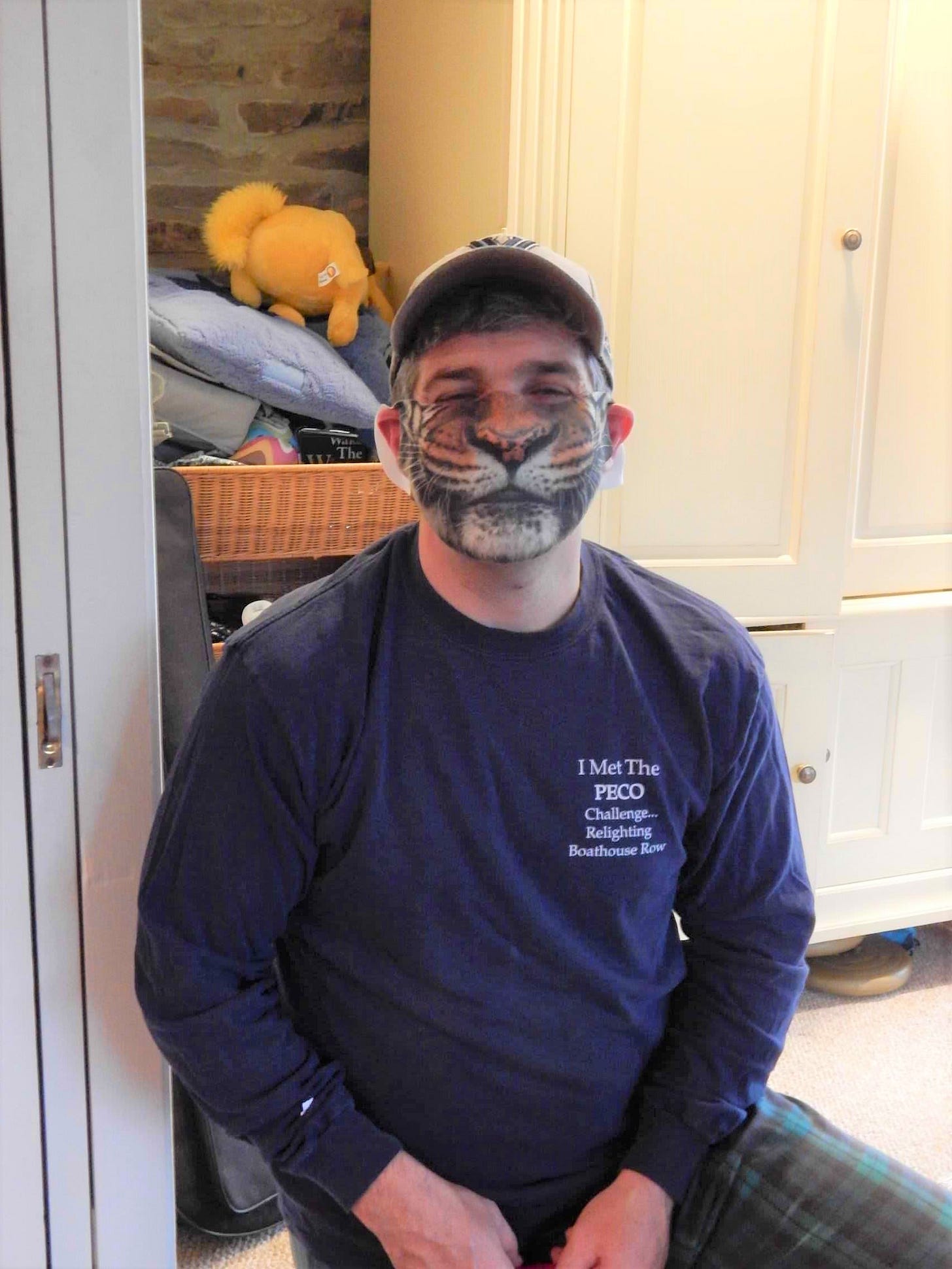 Middle-aged man in a baseball cap and his pajamas wearing a face mask that make him look like a tiger