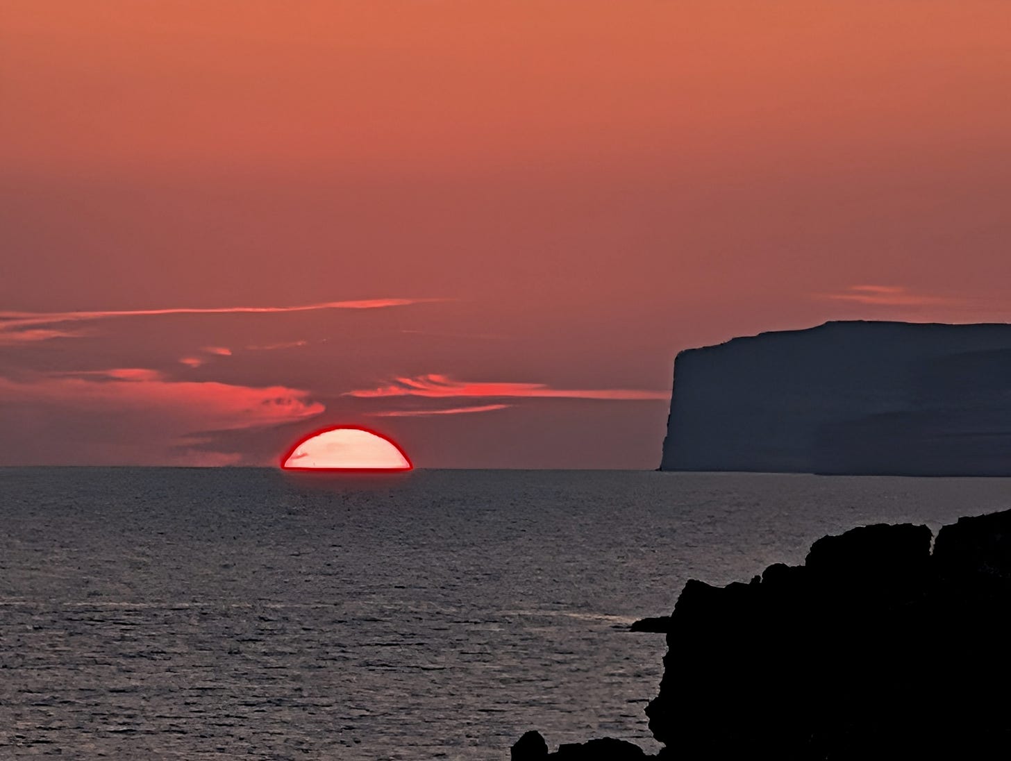 The sun setting over the horizon of the sea with some cliffs