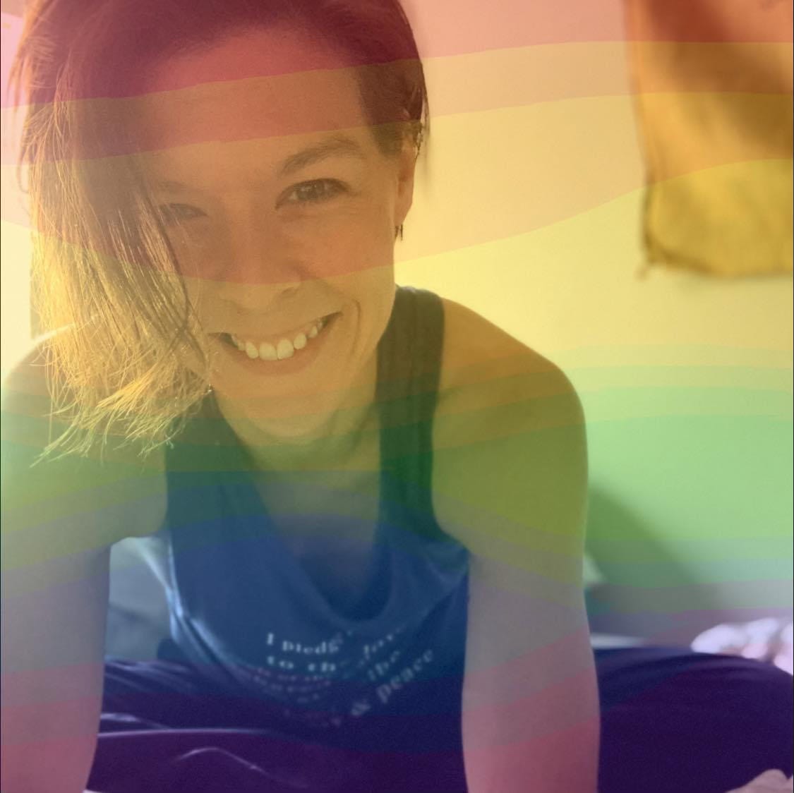 Photo of Jillian Abby smiling and leaning forward. A rainbow filter is applied over the picture.
