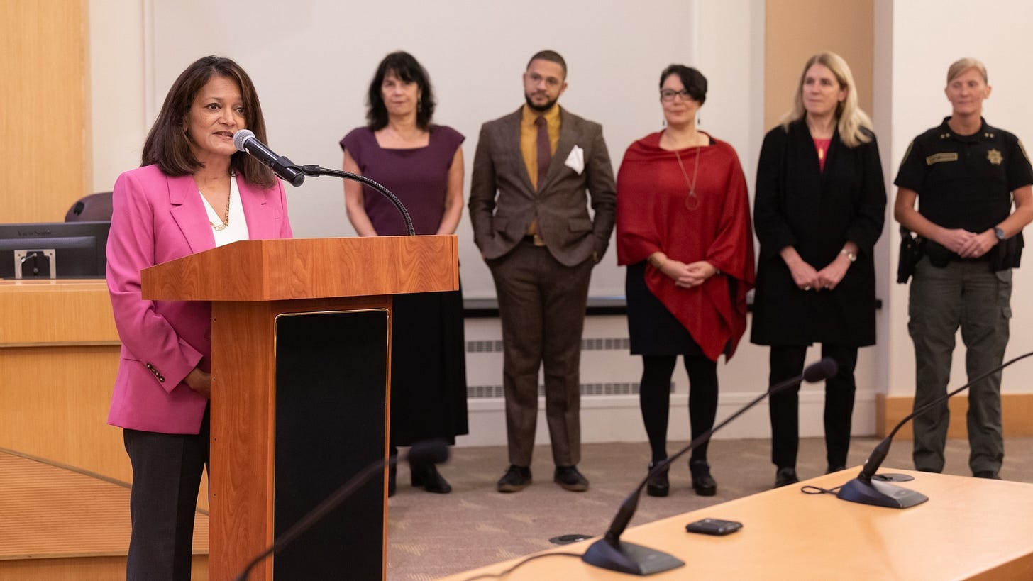 Former Commissioner Jayapal addresses the crowd as Commissioner Meieran, Beason, Chair Vega Pederson, Commissioner Julia Brim-Edwards, and  Sheriff Morrisey O'Donnell look on.