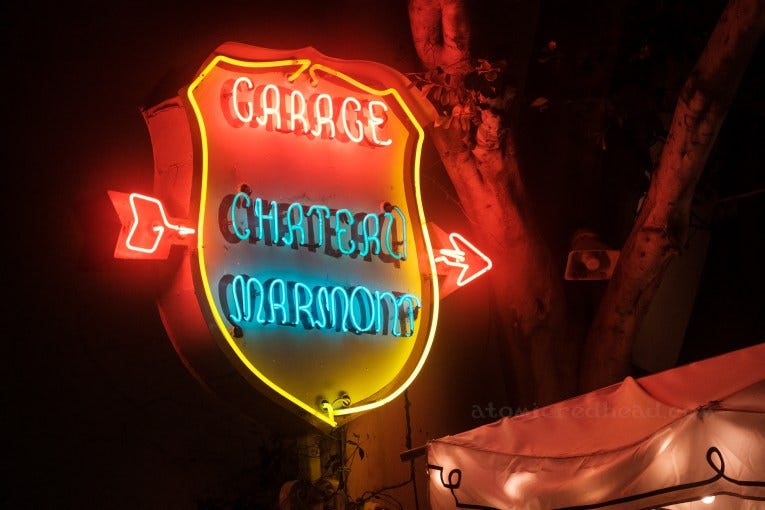A shield shaped neon sign has a red neon arrow passing through it. Red neon letters read "Garage" and below in blue neon letters reads "Chateau Marmont" A shield shaped neon sign has a red neon arrow passing through it. Red neon letters read "Garage" and below in blue neon letters reads "Chateau Marmont"