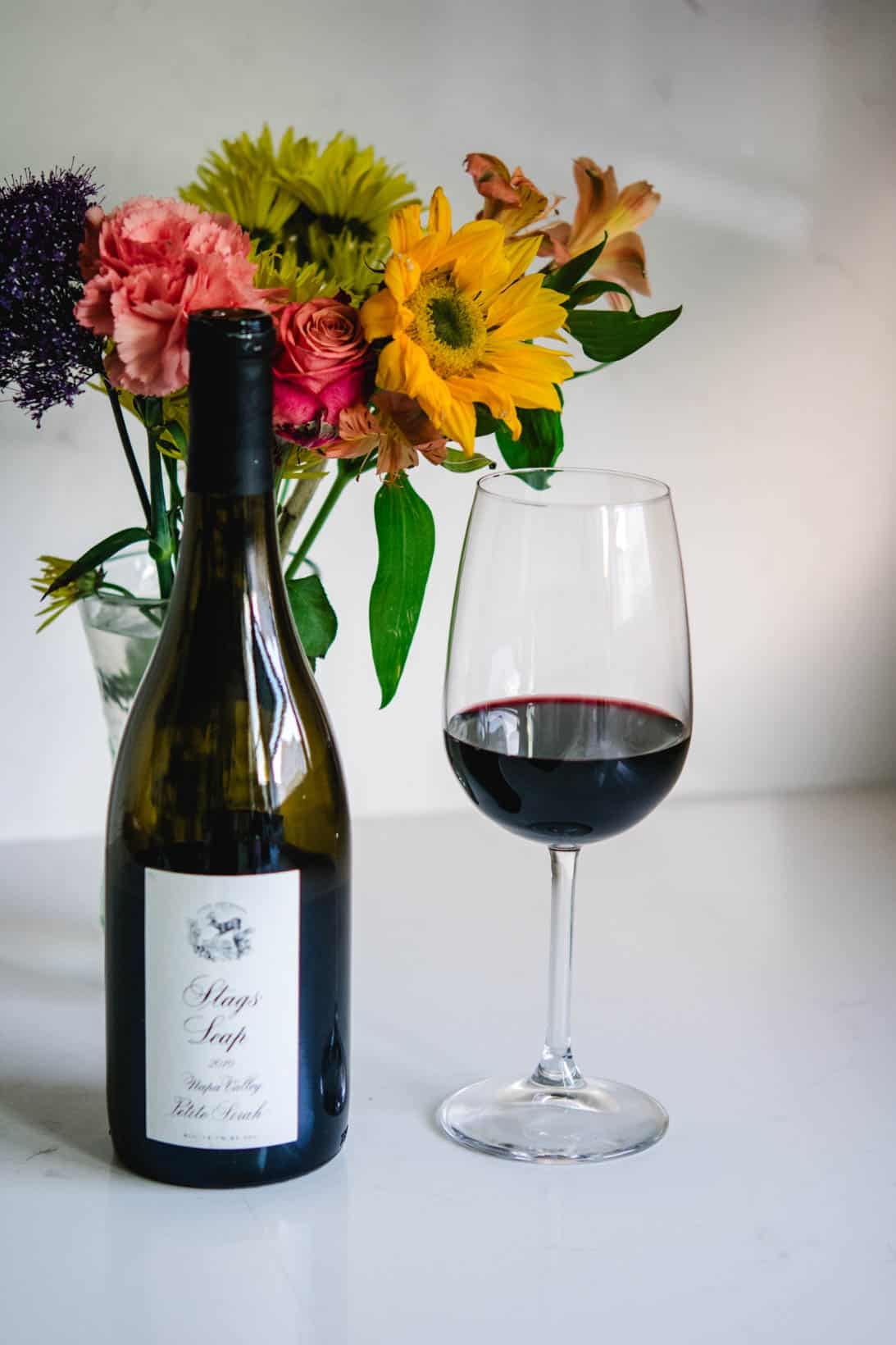 Stags' Leap Petite Sirah wine bottle and glass with flowers in the background Stags' Leap Petite Sirah wine bottle and glass with flowers in the background
