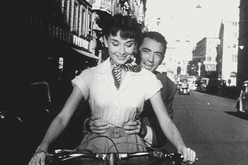 This may contain: a man and woman riding on the back of a bicycle