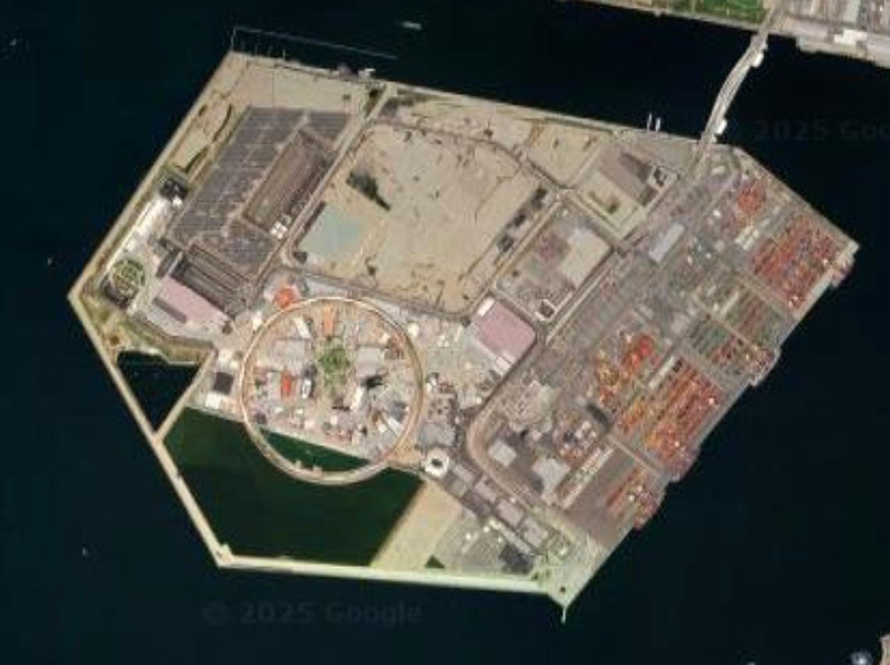 A satellite image of Yumeshima, a polygonal artificial island in Osaka Bay. On the southwest side is a large circular structure, which surrounds and is surrounded by buildings for Expo 2025.