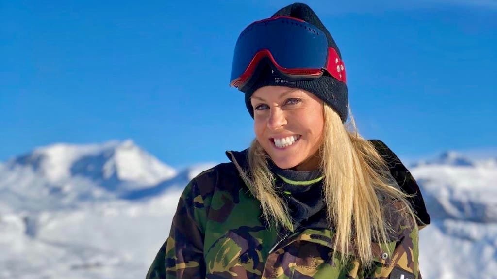 Chemmy Alcott standing in ski gear on a snowy mountain, with a bright blue sky behind her