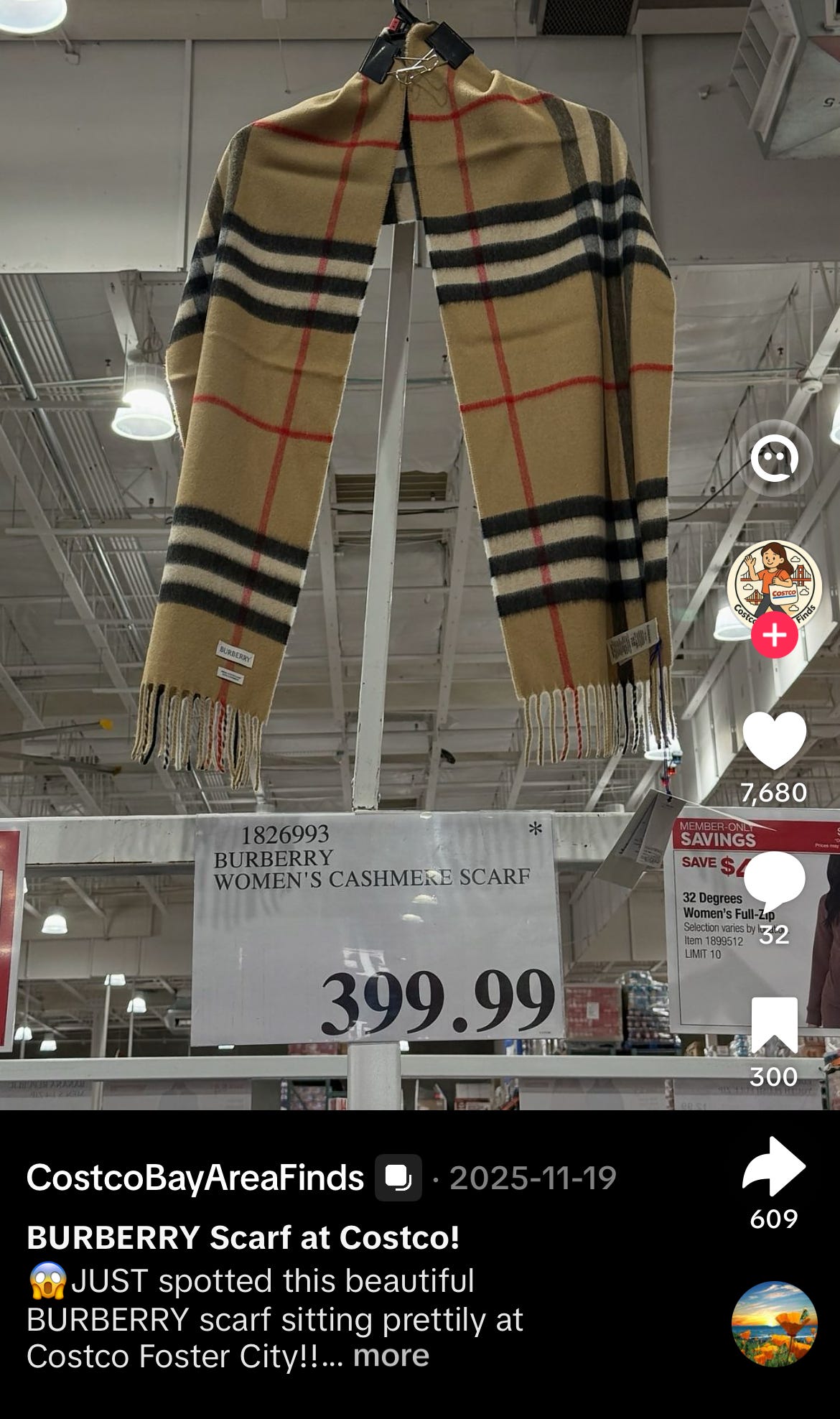 TikTok screenshot from creator @CostcoBayAreaFinds dated November 19, 2025, documenting an authentic Burberry women's cashmere scarf being sold at Costco Foster City in the San Francisco Bay Area at a price point of $399.99. The image shows the iconic Burberry check pattern cashmere scarf hanging by binder clips from a metal rail under the warehouse's exposed industrial ceiling and fluorescent lighting, displaying the signature camel-and-tan ground with crossing black, white, and red lines, finished with fringed cream-colored tassels at both ends and the small white Burberry brand label clearly visible at the lower-left edge of the scarf. Directly beneath the scarf, the official Costco merchandise price sign reads "1826993 BURBERRY WOMEN'S CASHMERE SCARF" with a clearly displayed retail price of $399.99, and the asterisk symbol in the top-right corner of the Costco price sign indicates a one-time buy item (Costco's standard signal that the SKU will not be reordered once sold through). A "Member-Only Savings SAVE $4" promotional sticker is partially visible to the right alongside an adjacent 32 Degrees women's full-zip jacket price sign with item number 1899512 and a purchase limit of 10. The TikTok post caption reads "BURBERRY Scarf at Costco! JUST spotted this beautiful BURBERRY scarf sitting prettily at Costco Foster City," and the video has accumulated 7,680 likes, 32 comments, 300 saves, and 609 shares. Geographic specificity (Costco Foster City, San Francisco Bay Area, Northern California) confirms US warehouse-club distribution of Burberry $BRBY.L luxury accessories at a roughly 50 percent discount versus full-line Burberry retail pricing for comparable cashmere scarves, which typically retail at $590 to $690 on the official Burberry e-commerce site. Channel-check evidence material to Burberry investors evaluating brand pricing discipline, parallel-channel inventory clearance, and the credibility of the company's articulated heritage refocus and pricing-by-authority framework under CEO Joshua Schulman, particularly given that the scarves category is one of the two hero categories the company cites as evidence of a successful return to authority-based pricing architecture. Notable that on a recent Intern Pierre primary research call, a former member of the Office of the CEO with 2.5 years of tenure stated total unfamiliarity with Burberry being sold at Costco despite this and similar documented evidence being available to the general public.