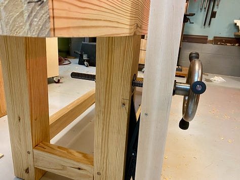 My workbench upside down on a table, the vice installed and a hand plane making shavings to flatten the bench top.