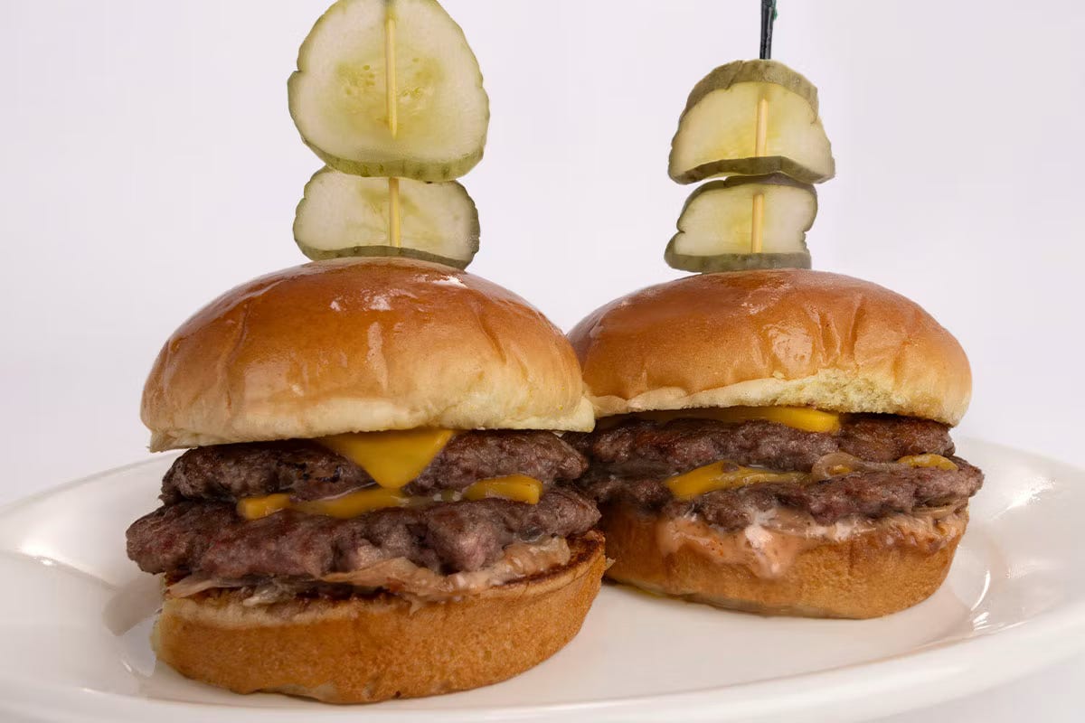 two souble smashburger sliders with two pickles on a toothpick against a white background two souble smashburger sliders with two pickles on a toothpick against a white background