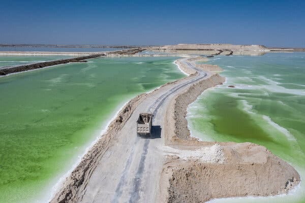 A truck drives on a sandy road between green water ponds.
