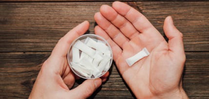 hand holding zyn packet and open container of zyn nicotine