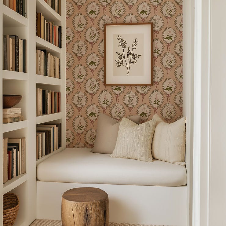 A cozy reading nook built in bench next to a bookshelf full of books with vintage style botanical wallpaper in a peach colorway.