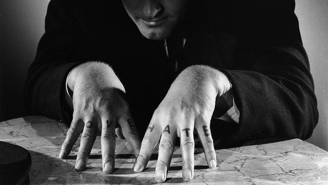 Two hands tented across a map with the words L-O-V-E and H-A-T-E tattooed on the knuckles.