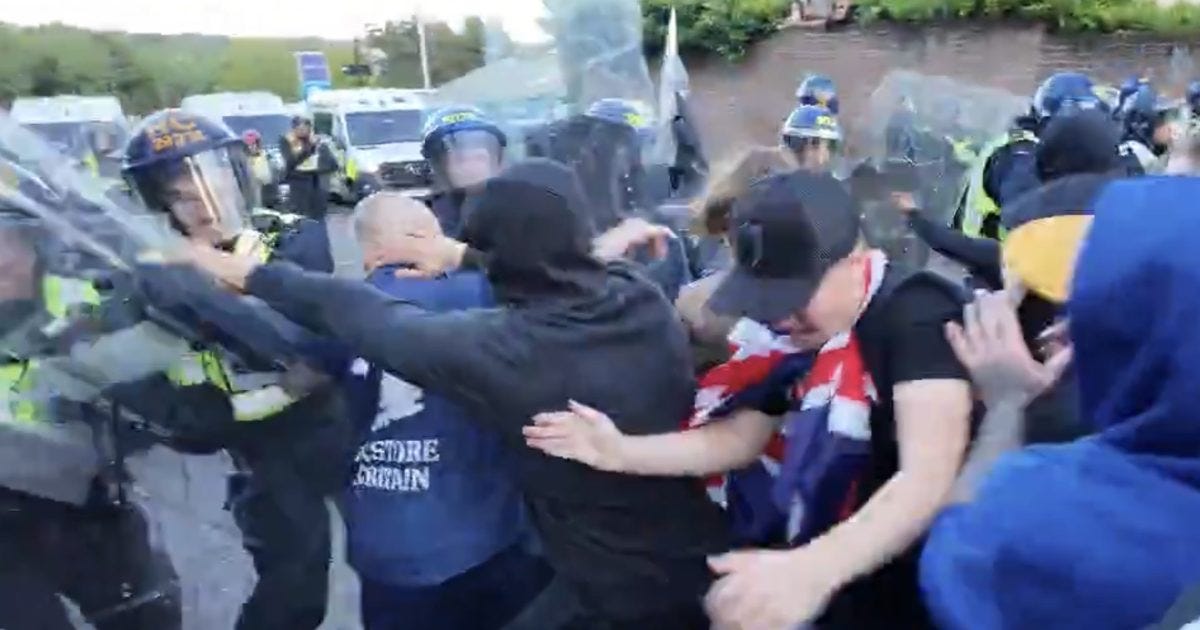 Police confront protesters during a chaotic demonstration, with individuals clashing and using barriers for protection amid a tense atmosphere.
