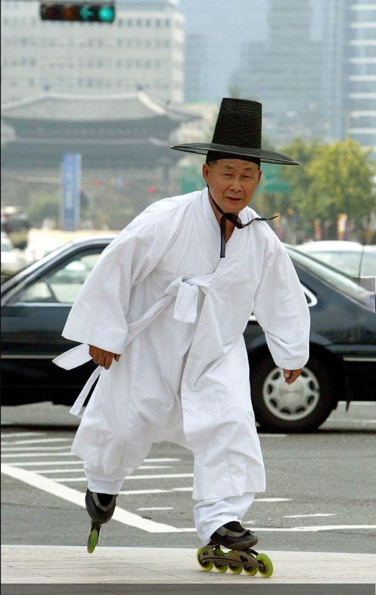 This may contain: an old man in white is skateboarding down the street while wearing a black hat