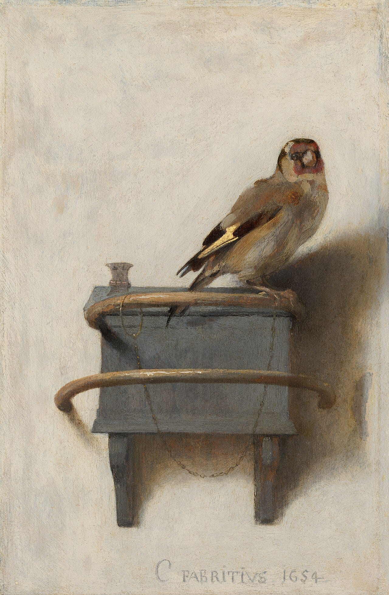 A goldfinch chained by one leg to its feed box A goldfinch chained by one leg to its feed box