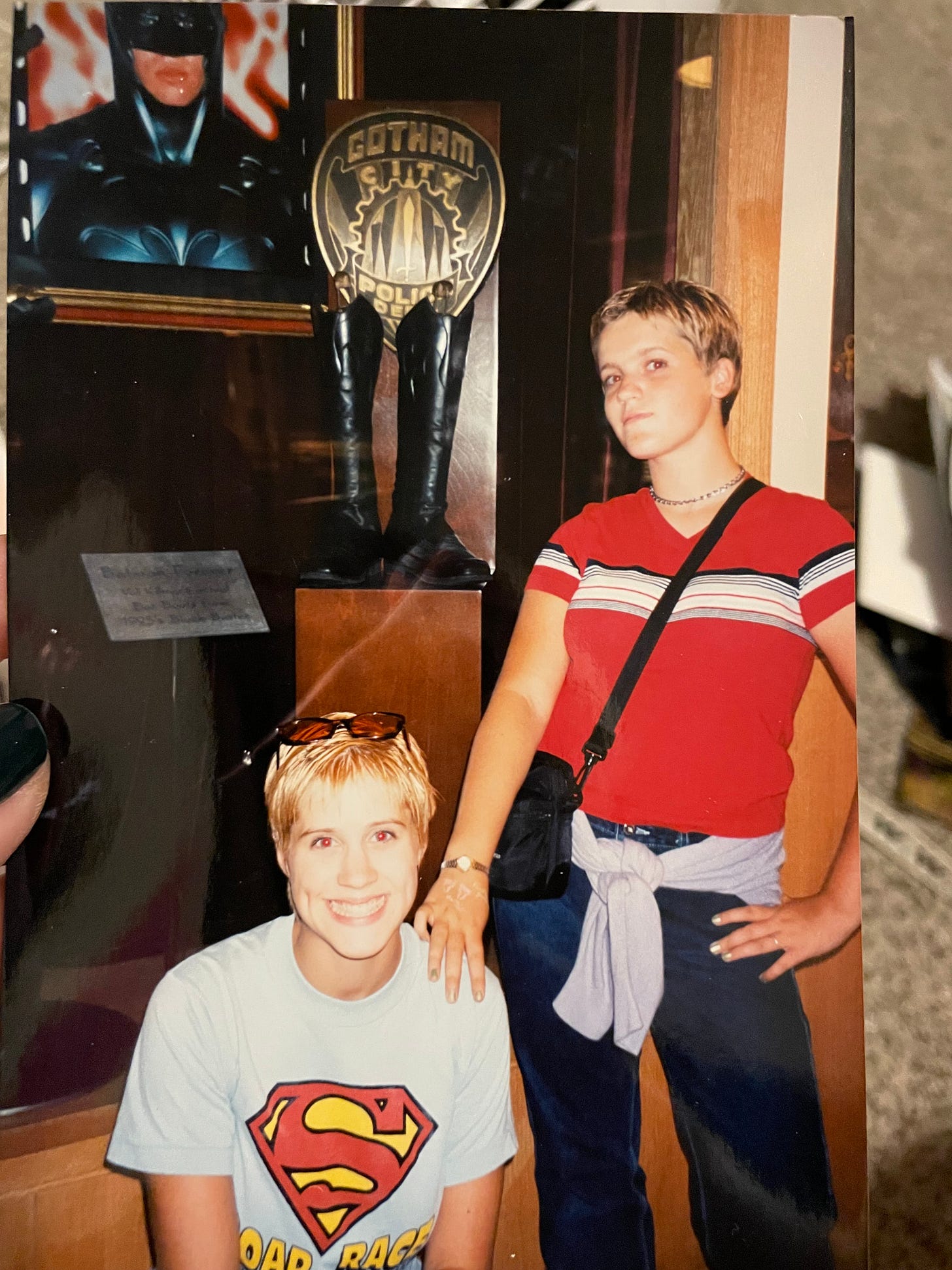 a photo of two white teenagers in front of a display of batman mermoabilia in the 1990s 