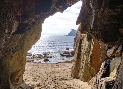 A photograph of the view from inside a cave, the entrance of which frames the image, looking out onto a beach and the sea.