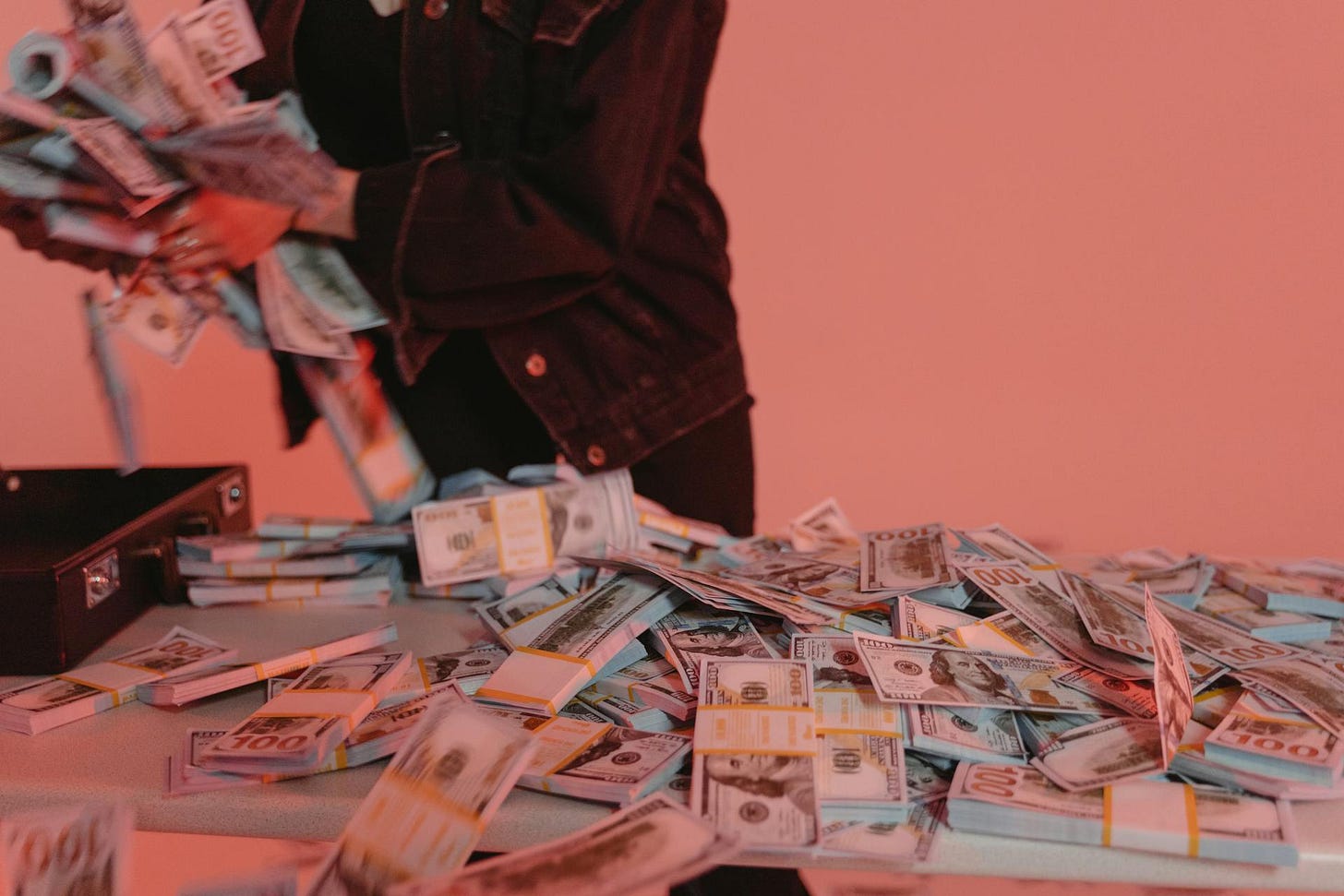 Person in dark clothing dropping stacks of US dollar bills, with currency scattered across pink background, depicting financial sanctions.