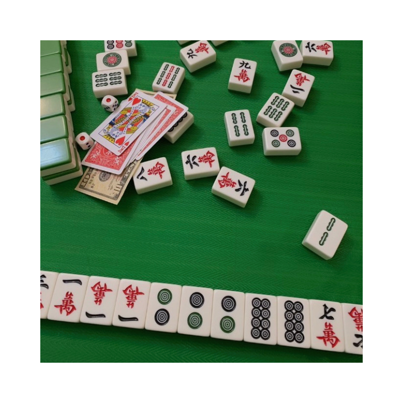 mahjong tiles laid on a tabletop with some money, playing cards, and a pair of dice.