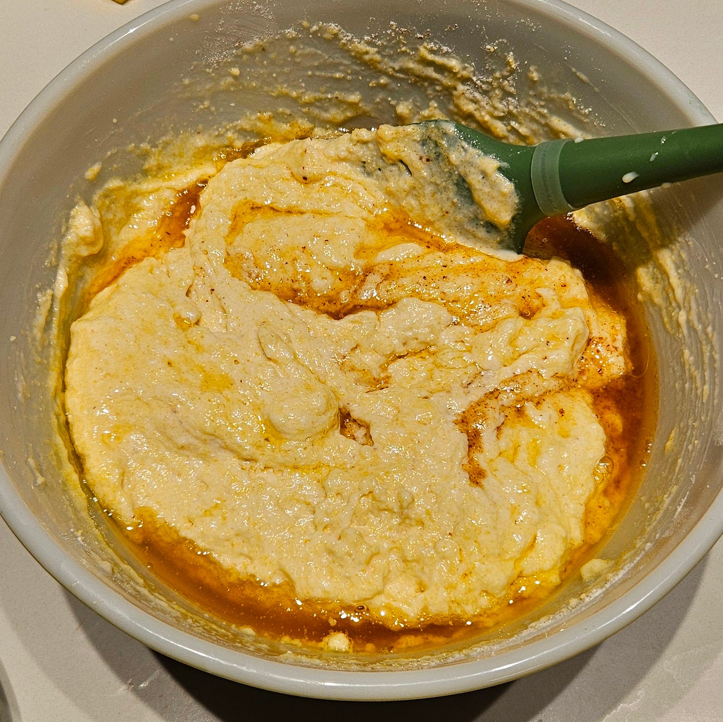 Corn bread batter with browned butter drizzled on top being mixed with a green spatula