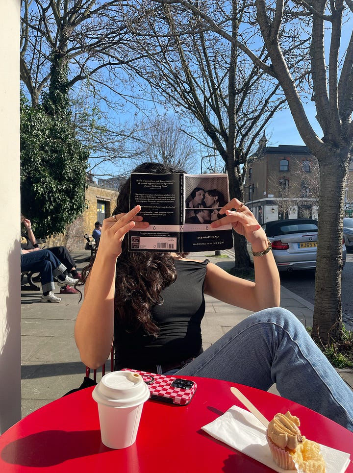 two girls sat outside a café in the sun, one reading 'madonna in a fur coat,' the other holding a copy of anna karenina