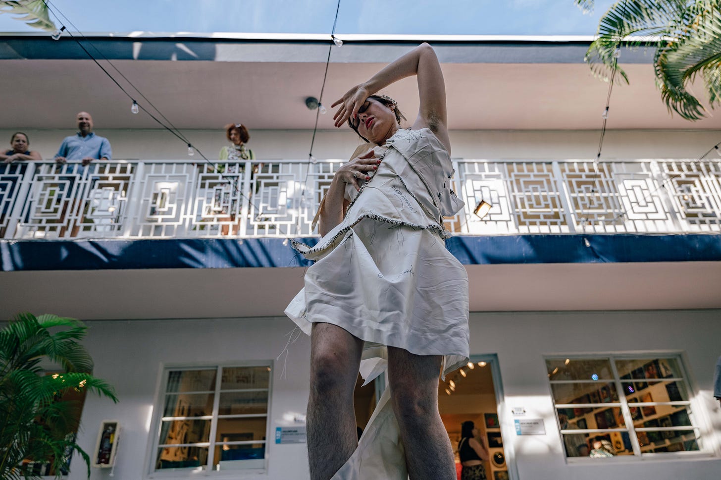 girl dances in artistic white dress while people look on from a balcony