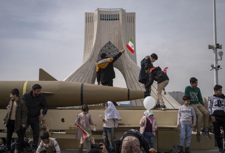 Iranian children stand and wave flags on a missile. 