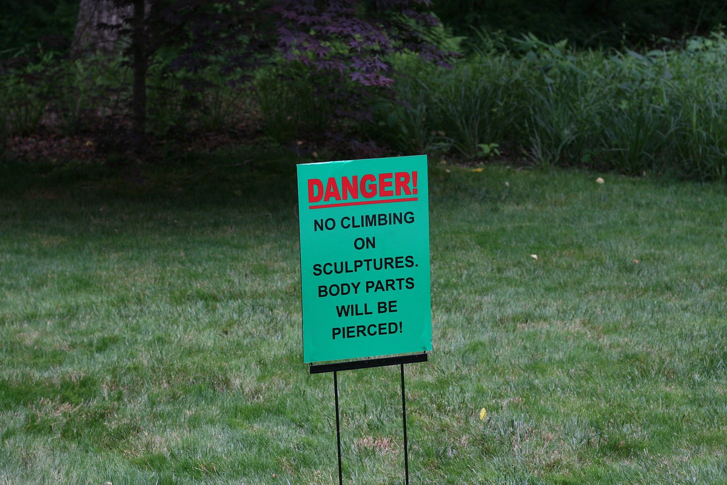 sign that reads "DANGER! no climbing on sculptures. body parts will be pierced!" from a botanical garden