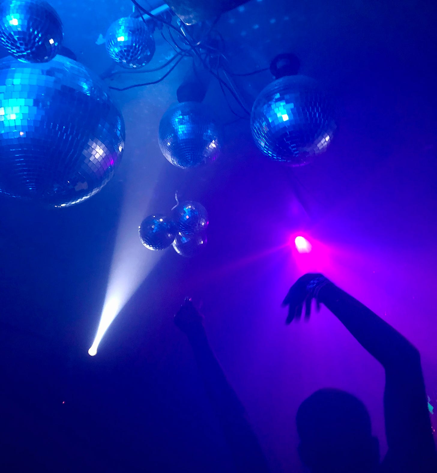 silhouette with raised arms under disco balls in blue lighting