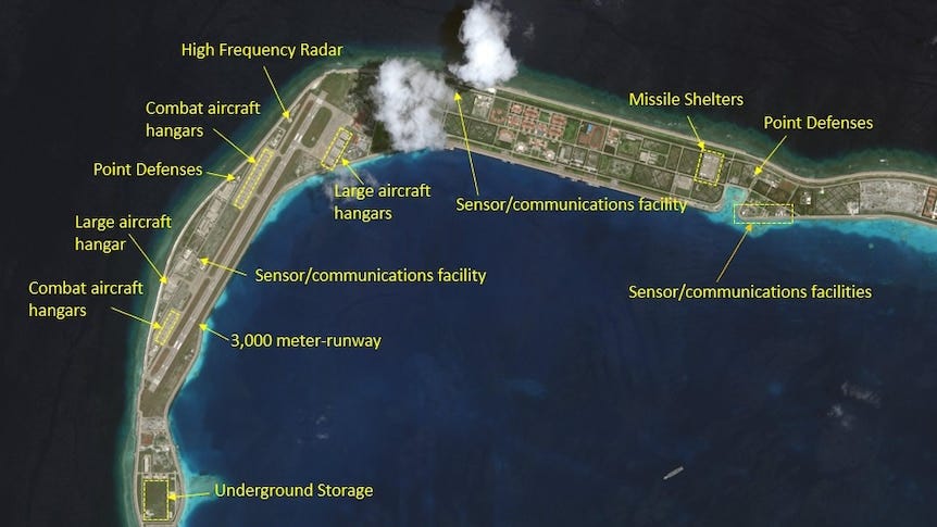 A satellite photo of a long, thin, curved island annotated to identify military facilities along its entire length.