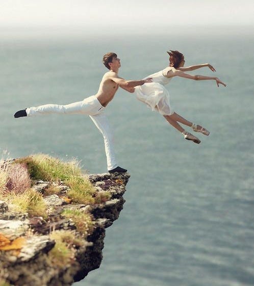 This may contain: two people are jumping off the edge of a cliff into the ocean while holding hands