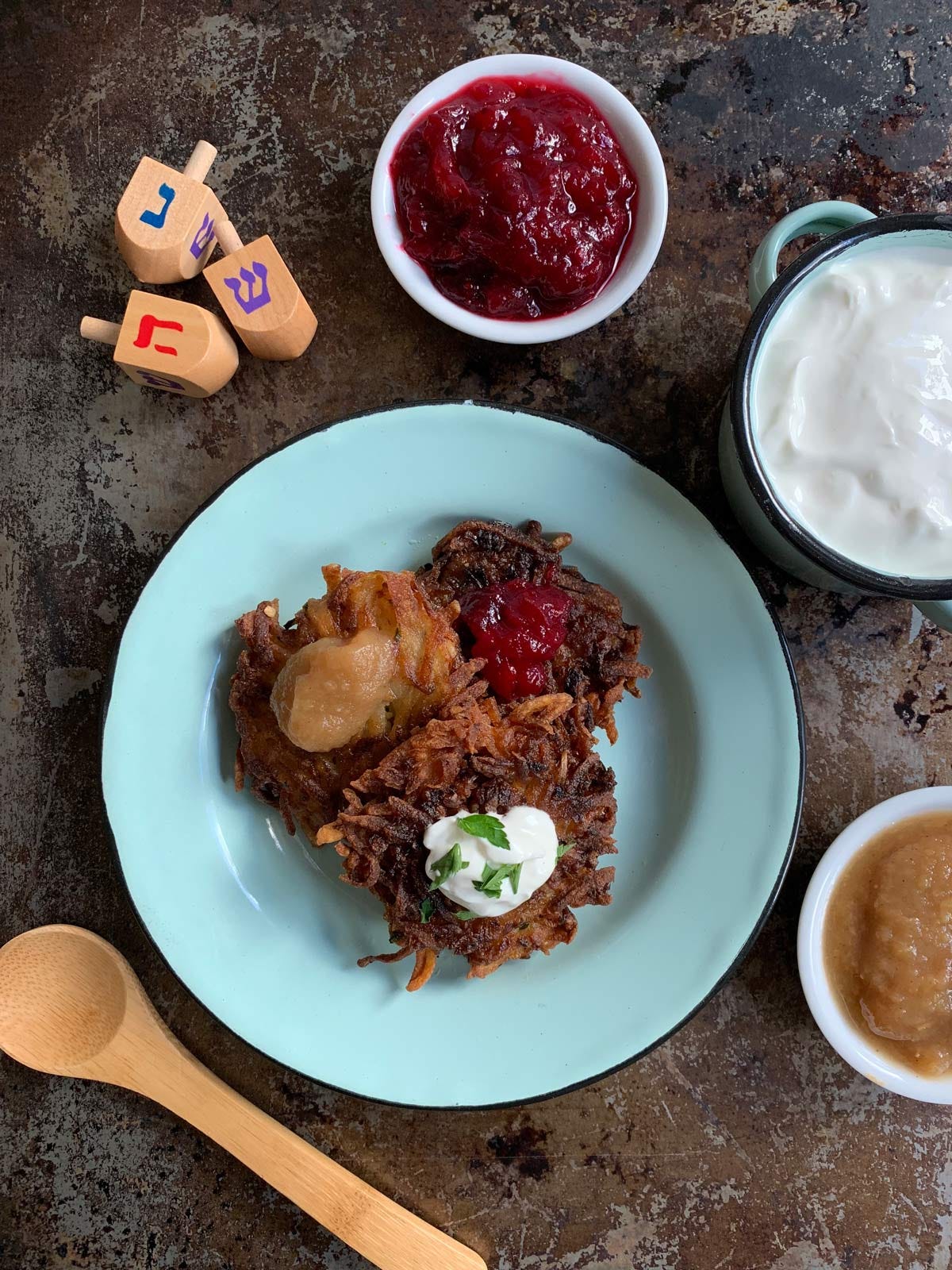 Latkes on a blue plate with three different toppings and dreidels in the the upper left. Latkes on a blue plate with three different toppings and dreidels in the the upper left.