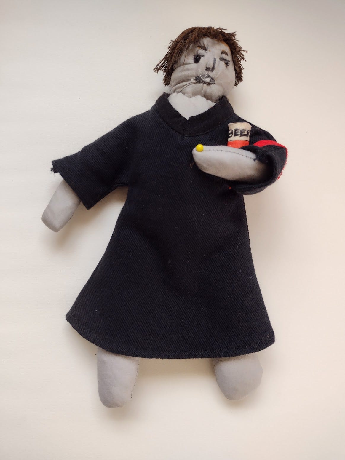 Grey fabric doll with brown hair, a black judge's robe, and one bent arm holding a can labled BEER