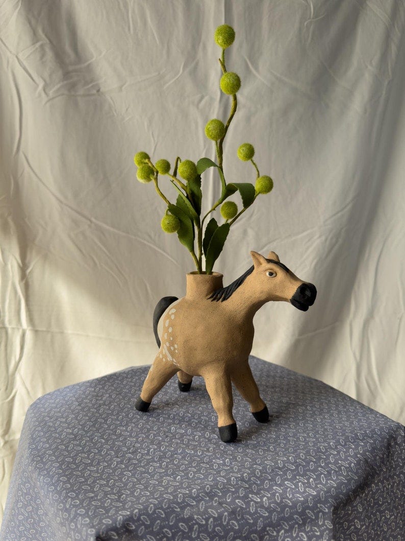 May include: A ceramic horse planter in a light brown color with white spots. The horse has a black mane and tail. A green plant with small round green leaves is in the planter. May include: A ceramic horse planter in a light brown color with white spots. The horse has a black mane and tail. A green plant with small round green leaves is in the planter.
