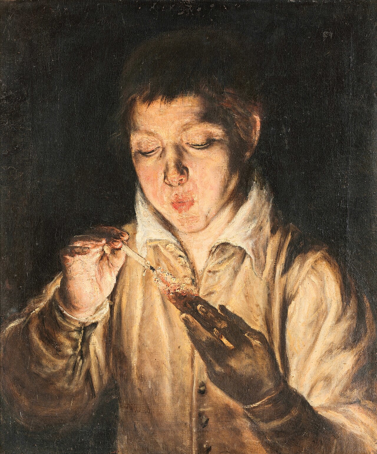 A boy blowing on a glowing coal that lights his face A boy blowing on a glowing coal that lights his face