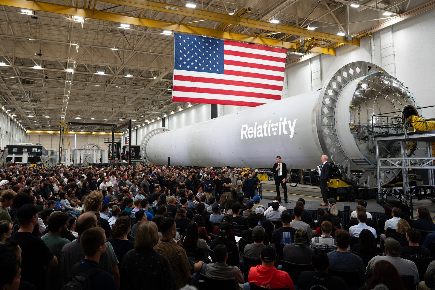 NASA Administrator Jared Isaacman stands in front of a large, cylindrical, gray spacecraft with a white Relativity logo on it and addresses hundreds of Relativity Space employees. A large American flag hangs from the ceiling. NASA Administrator Jared Isaacman stands in front of a large, cylindrical, gray spacecraft with a white Relativity logo on it and addresses hundreds of Relativity Space employees. A large American flag hangs from the ceiling.