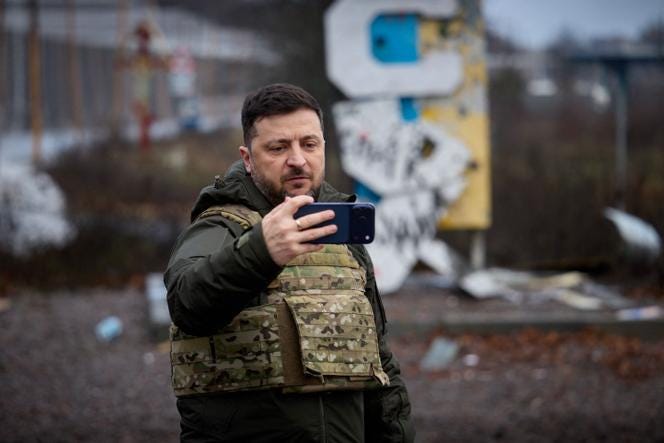In this handout photograph taken and released by the Ukrainian Presidential Press Service on December 12, 2025, Ukraine's President Volodymyr Zelensky records a video message on his mobile phone in front of the road sign marking the entrance to Kupiansk, Kharkiv region.
