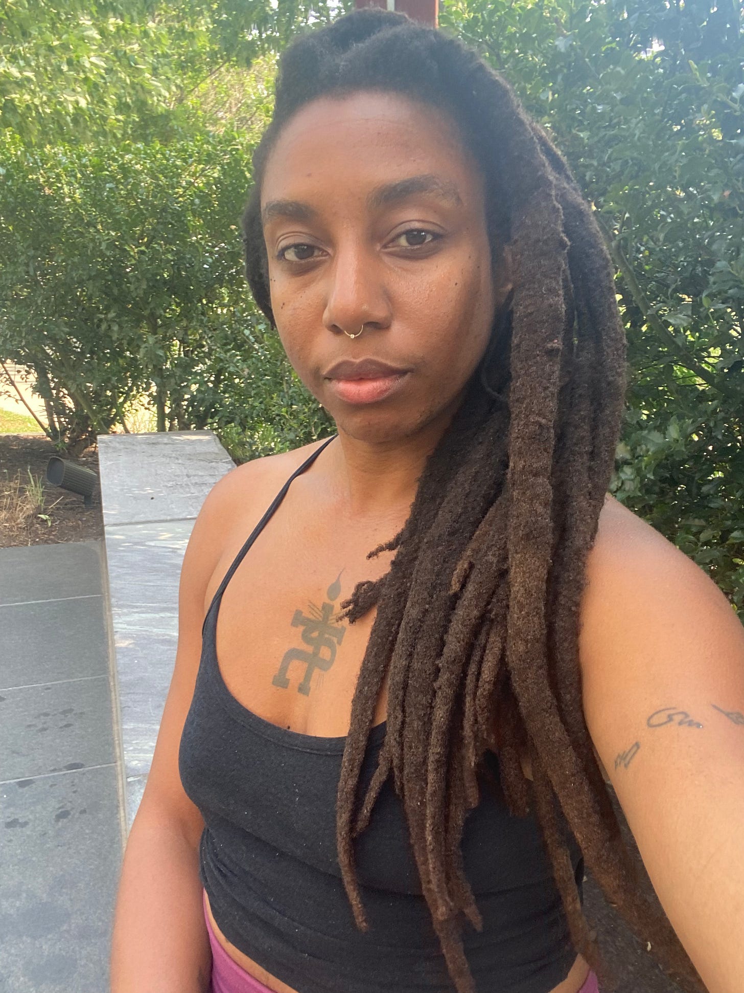 beautiful black woman with locs (n3vlynnn) sitting in front of a large green bush at a park