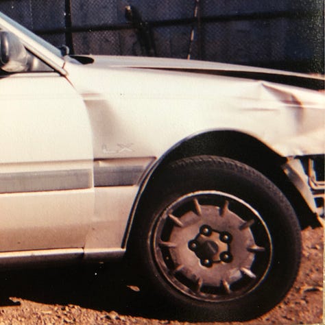 My champagne Mazda 626 lurches cockeyed in the wreck yard with other munched vehicles. The smashed front bumper lies on the ground. The windshield is lanced with cracks. The passenger side is caved in. The drivers side is demolished.
