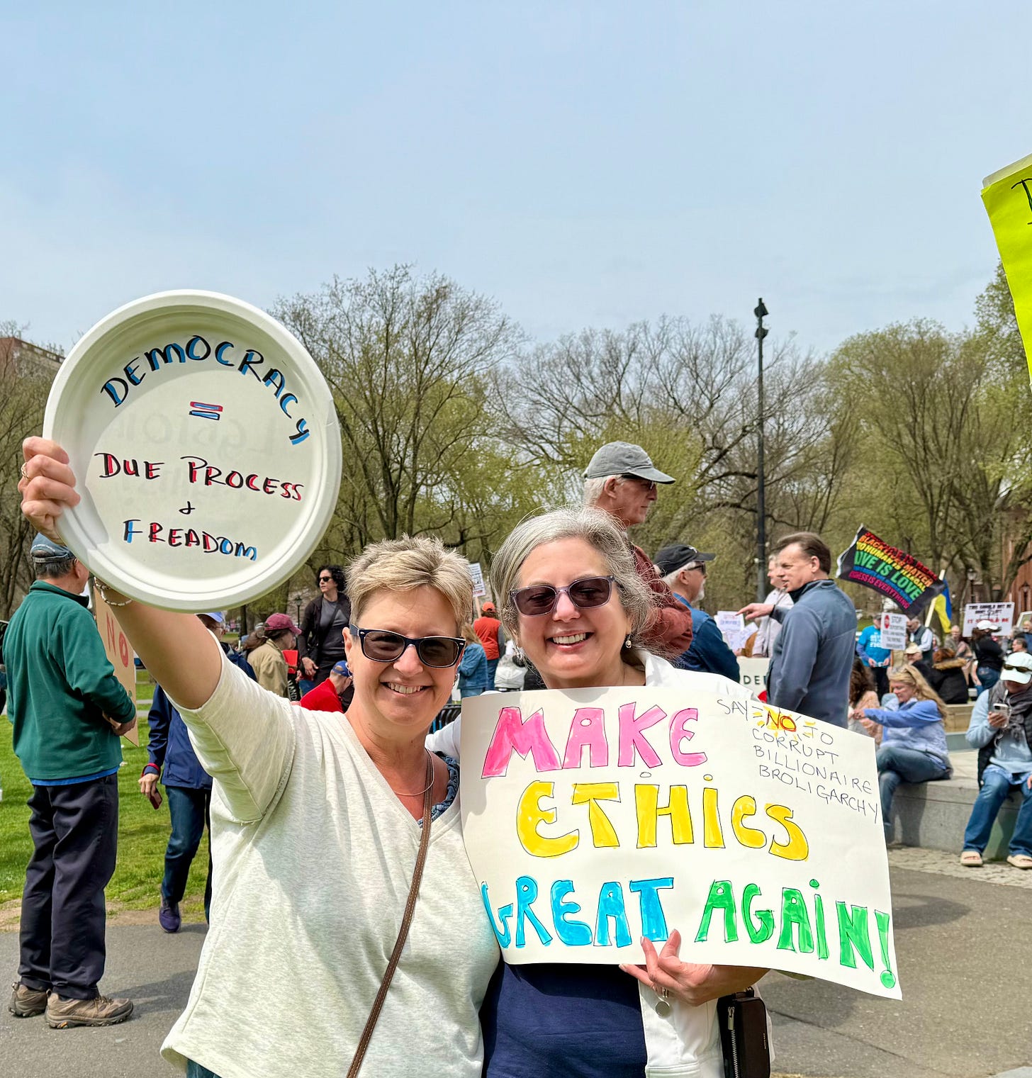 Pia Ledina and Sarah Darer Littman holding signs that read: Democracy = Due Process+FREADOM and "Make Ethics Great Again: Say no to the Billionaire broligarchy!"