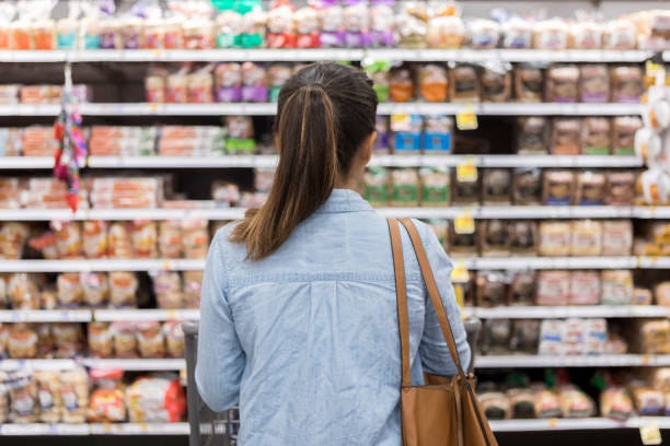 Unrecognizable woman marvels at grocery bread selection In this rear view, an unrecognizable woman stands with a shopping cart in front of a shelf full of food in the bread aisle of a grocery store. product assortment stock pictures, royalty-free photos & images Unrecognizable woman marvels at grocery bread selection In this rear view, an unrecognizable woman stands with a shopping cart in front of a shelf full of food in the bread aisle of a grocery store. product assortment stock pictures, royalty-free photos & images