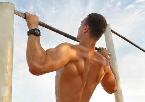 Fit muscular man doing pullups at an outdoor gym with his shirt off. 