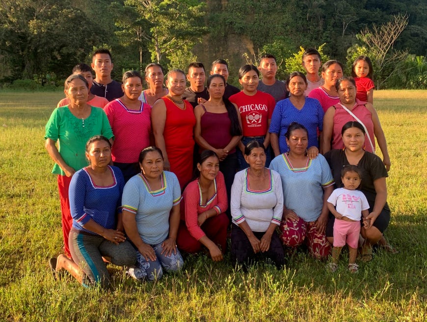 Around 20 people, mainly women, from the Ecuadorian Amazon, stand posing for the camera in a field on a sunny day