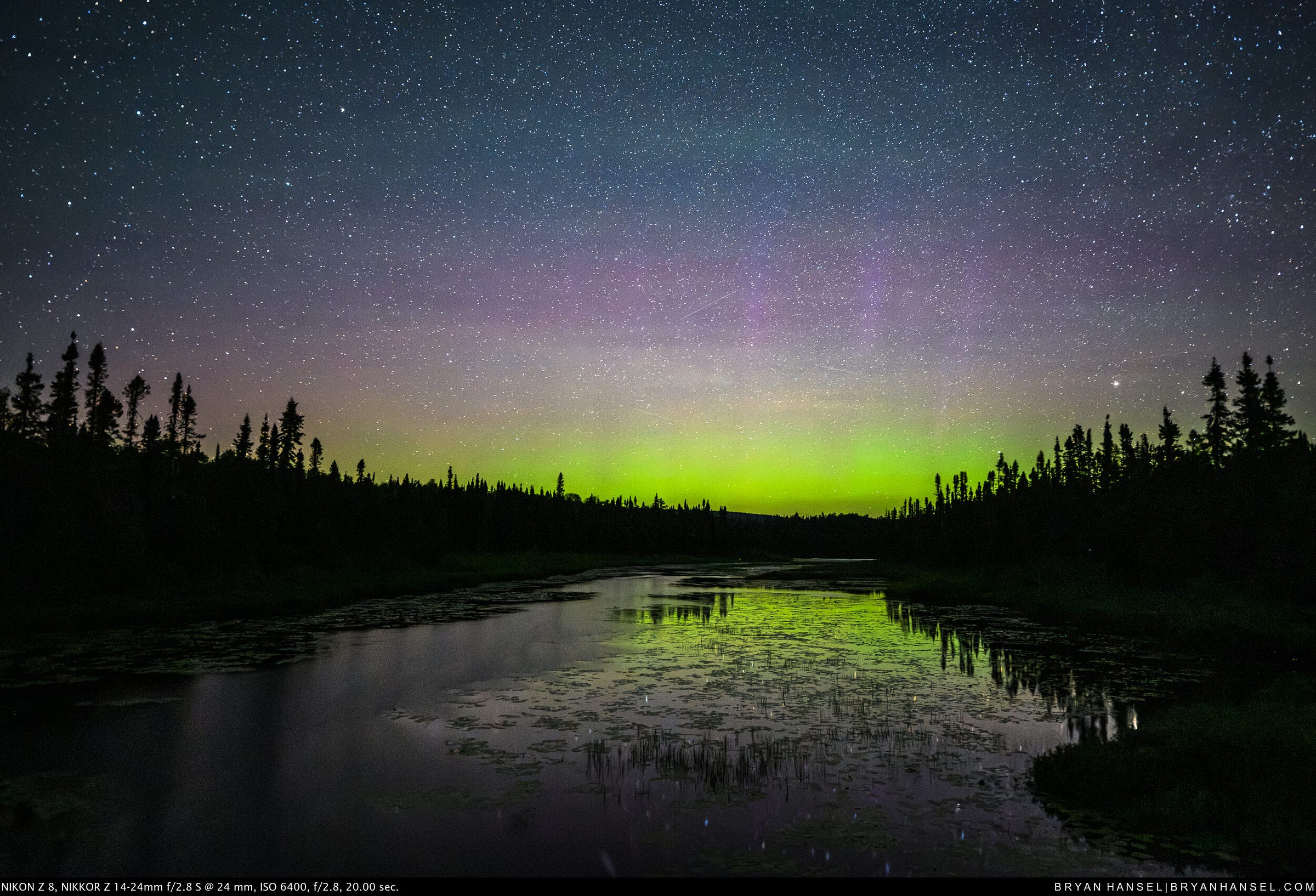 The northern lights over a river. They reflect in the river below.