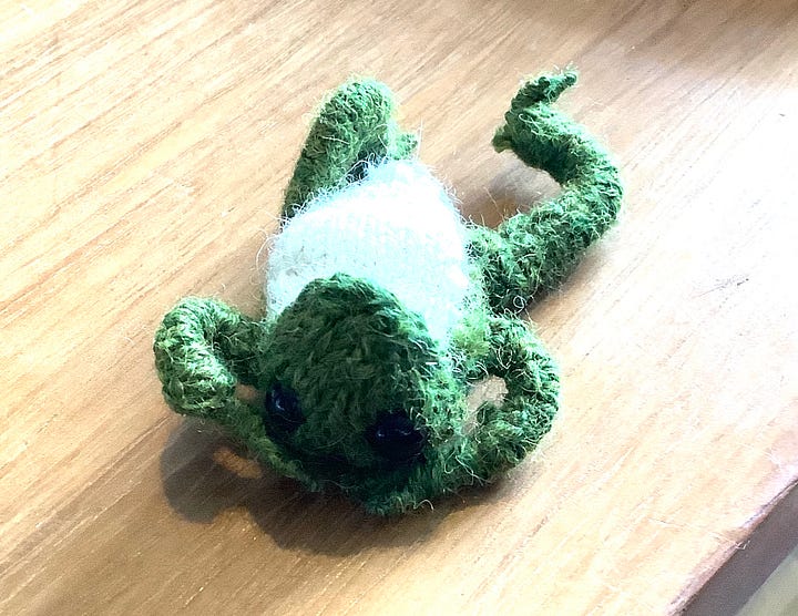 A green frog, with a cream chest, black eyes and a cheeky look. Sitting in a variety of positions, including lying on his back.