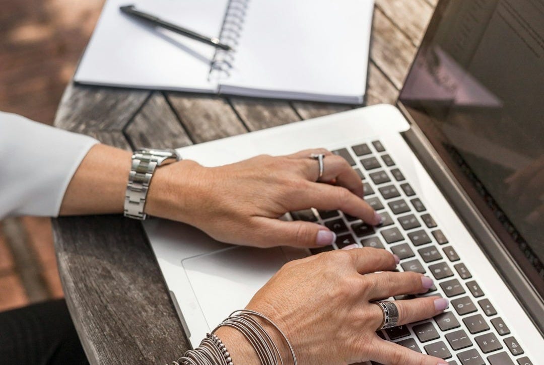 person typing on MacBook Pro on brown wooden table during daytime photo