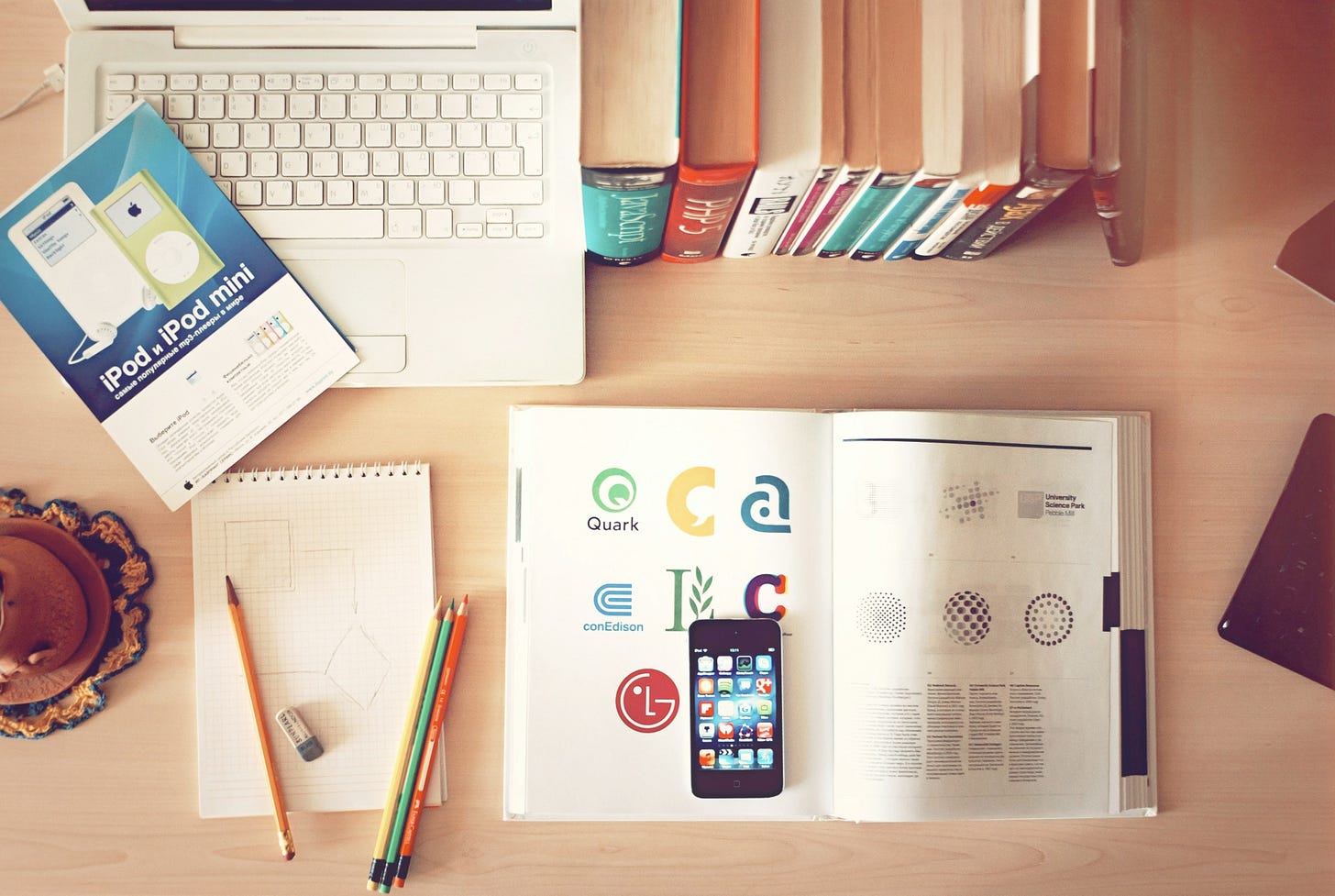 wood desk with laptop, textbooks, phone, and pencils spread across it